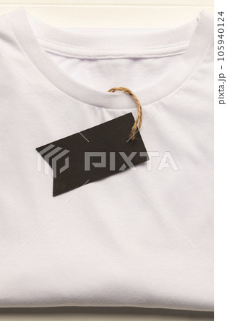 Close up of flat lay of white t shirt with tag and copy space on white boards background Close up of flat lay of white t shirt with tag and copy space on white boards background 105940124
