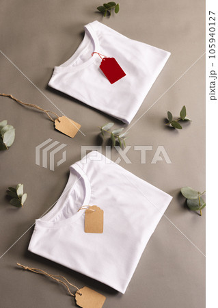 Folded white t shirts with tags and leaves with copy space on brown background Folded white t shirts with tags and leaves with copy space on brown background 105940127