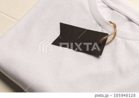 Close up of flat lay of white t shirt with tag and copy space on white boards background Close up of flat lay of white t shirt with tag and copy space on white boards background 105940128