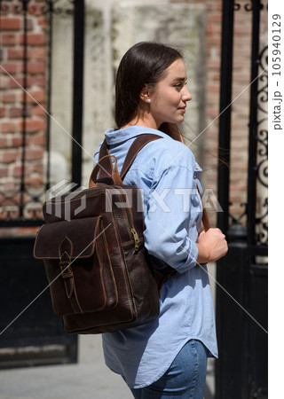 Beautiful young girl wearing blue jeans, shirt and white t-shirt posing with brown leather backpack Beautiful young girl wearing blue jeans, shirt and white t-shirt posing with brown leather backpack 105940129