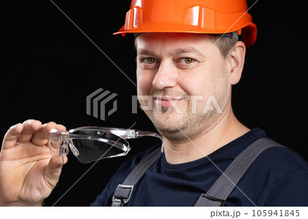 Portrait of a handsome worker builder in overalls, helmet and glasses on a black background. 105941845