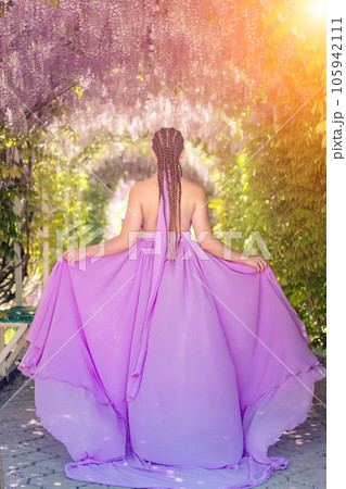 Woman wisteria lilac dress. Thoughtful happy mature woman in purple dress surrounded by chinese wisteria 105942111