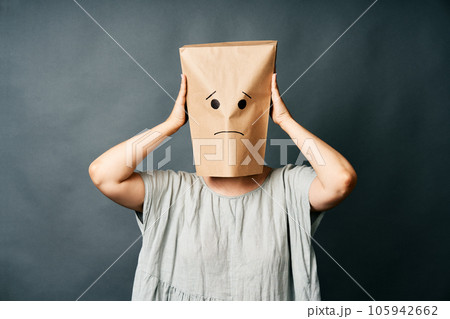 Upset woman with a paper bag on head touching temples, suffering from strong tension headache 105942662