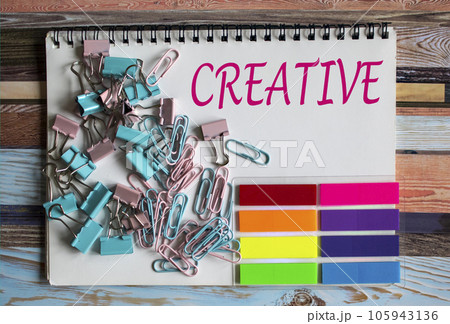 The text on the notebook is Creative. Nearby are paper clips, colored stickers. The text on the notebook is Creative. Nearby are paper clips, colored stickers. 105943136