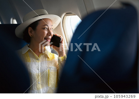 Positive middle aged woman tourist passenger talking on mobile phone and looking through airplane window. 105943269