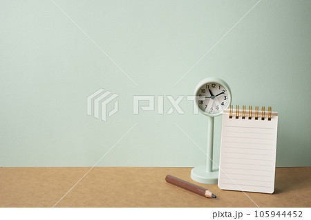 Notebook, colored pencil, clock on brown desk. mint green wall background. workspace, copy space Notebook, colored pencil, clock on brown desk. mint green wall background. workspace, copy space 105944452