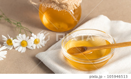 Chamomile syrup in a small bowl and in a jar and chamomile flowers on a linen kitchen towel 105946513