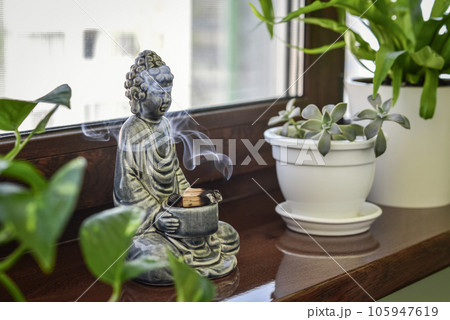 Candlestick in the shape of a buddha, smoldering Palo Santo and houseplants 105947619