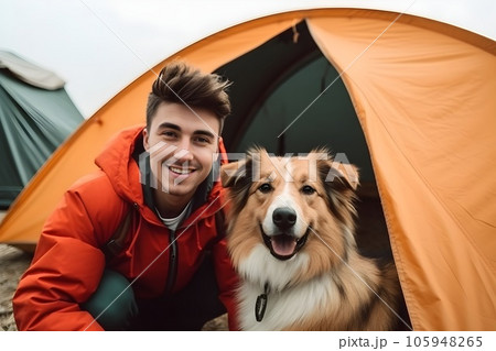 Happy young man is sitting with his dog by a tourist tent. Traveling together with pets concept. AI generated. 105948265