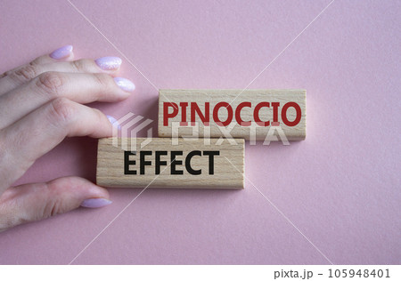 Pinoccio Effect symbol. Concept word Pinoccio Effect on wooden blocks. Businessman hand. Beautiful pink background. Business and Pinoccio Effect concept. Copy space Pinoccio Effect symbol. Concept word Pinoccio Effect on wooden blocks. Businessman hand. Beautiful pink background. Business and Pinoccio Effect concept. Copy space 105948401