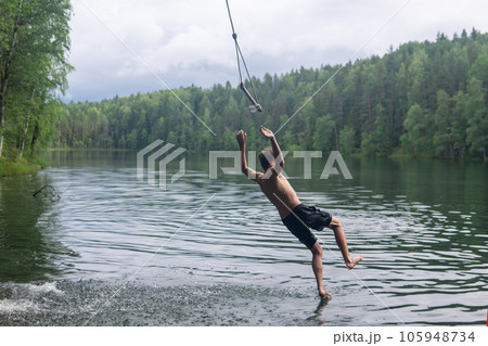 boy jumps into the water using a tarzan swing while swimming in a forest lake 105948734