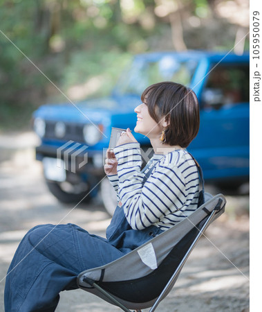 青い車をバックにアウトドアチェアに座って飲み物を飲む女性 青い車をバックにアウトドアチェアに座って飲み物を飲む女性 105950079