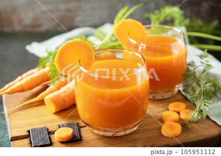 Carrot juice in a glass and fresh carrots with leaves on a stone table. Carrot healthy juice for detox. Healthy vegan vegetarian drink. 105951112