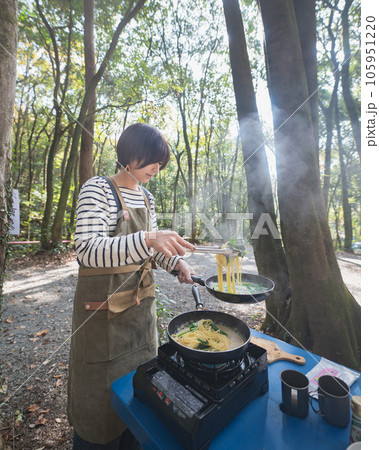木漏れ日の差すキャンプ場で料理をする女性 105951220