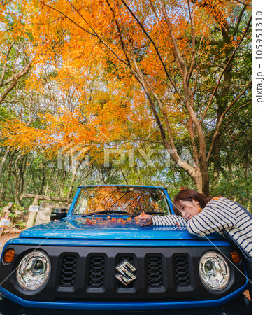 紅葉の中青い車のボンネットの上にもたれかかる女性 105951310