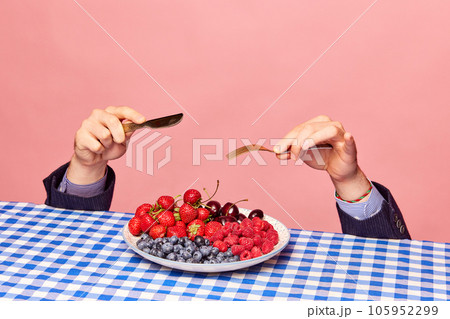 Male hands with knife and fork over plate with fresh berries against pink background. Vitamin mix 105952299