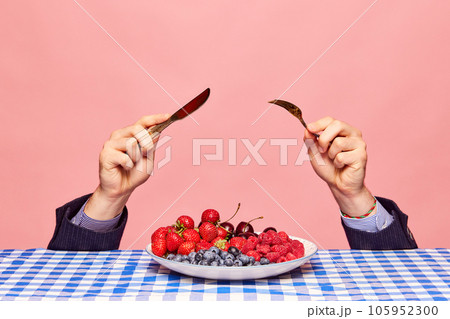 Male hands with knife and fork over plate with fresh berries against pink background. Vitamin mix 105952300
