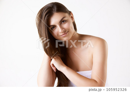 Portrait of beautiful brunette young woman with long straight hair, standing in towel against white studio background 105952326