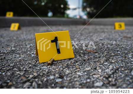 A group of yellow crime scene evidence markers on the street after a gun shooting brass bullet shell casing rifle A group of yellow crime scene evidence markers on the street after a gun shooting brass bullet shell casing rifle 105954223