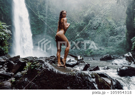 Woman near waterfall. Traveler nudist girl posing on waterfall with powerfull stream Woman near waterfall. Traveler nudist girl posing on waterfall with powerfull stream 105954318