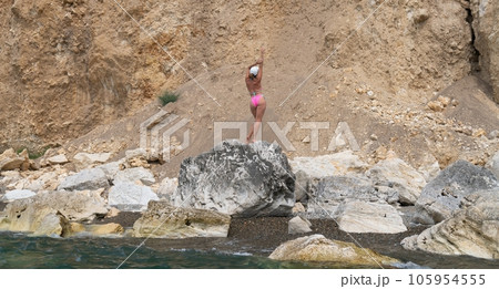 Woman travel sea. Happy tourist in pink bikini enjoy taking picture outdoors for memories. Woman traveler posing on the beach at sea surrounded by volcanic mountains, sharing travel adventure journey Woman travel sea. Happy tourist in pink bikini enjoy taking picture outdoors for memories. Woman traveler posing on the beach at sea surrounded by volcanic mountains, sharing travel adventure journey 105954555