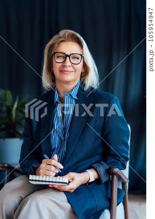 Professional Psychotherapy. Successful female Psychologist Smiling To Camera Sitting On armchair In Office. Mature 50s middle-age professional portrait of teacher, coach, mentor, therapist, counselor Professional Psychotherapy. Successful female Psychologist Smiling To Camera Sitting On armchair In Office. Mature 50s middle-age professional portrait of teacher, coach, mentor, therapist, counselor 105954947