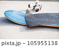 Applying grip tape to a brand new skateboard deck next to a set of trucks and wheels 105955138