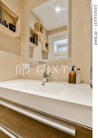 a modern bathroom with beige tile walls and white counters, along with a large mirror above the sink area a modern bathroom with beige tile walls and white counters, along with a large mirror above the sink area 105955683
