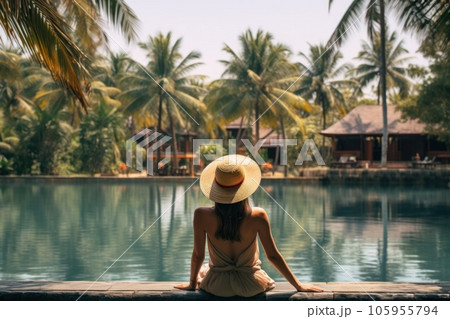 A woman wearing a hat looking at the water of a lagoon hotel and a swimming pool 105955794