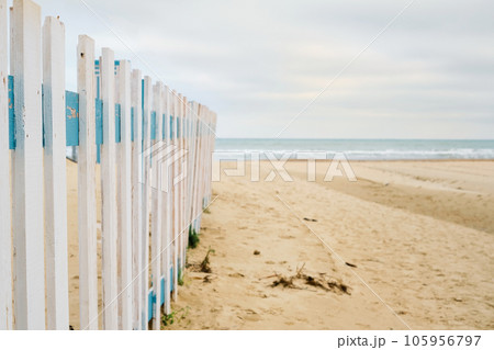 Deserted spring beach, fence in front of a public beach, cloudy sky in anticipation of rain. Off-season sea beach, place for text 105956797