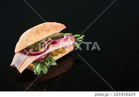 Dutch sandwich with herring and pickles pickled cucumber and red onion on the dark mirror table. Close up, selective focus and copy space Dutch sandwich with herring and pickles pickled cucumber and red onion on the dark mirror table. Close up, selective focus and copy space 105956824