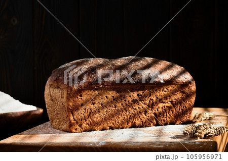 Homemade freshly baked whole grain bread made from rye and wheat sourdough, selective focus on a loaf of bread. Dark mood. Traditional techniques loave, innovating bread, slow carb baking 105956971