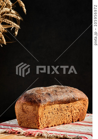 Freshly baked artisan whole grain bread from rye and wheat sourdough, on rustic gray kitchen towel, dark background. Vertical shot, selective focus on a loaf of bread Freshly baked artisan whole grain bread from rye and wheat sourdough, on rustic gray kitchen towel, dark background. Vertical shot, selective focus on a loaf of bread 105956972