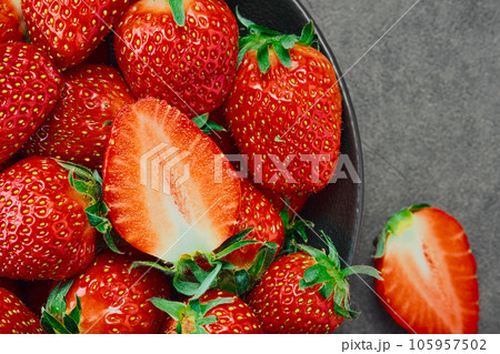 Freshly harvested summer strawberries, berry cut in half and whole berries. Ripe strawberries in a dark bowl top view. Background of ripe strawberries, delicious natural dessert 105957502