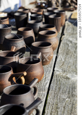 Many dark-colored clay pots stand on the table in pottery workshops. Sale of clay products. Many dark-colored clay pots stand on the table in pottery workshops. Sale of clay products. 105957554