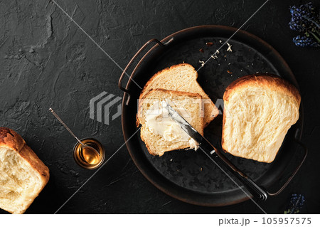 Sweet brioche bread on tray with knife , butter and honey on a dark vintage surface. Flat lay traditional sweet French brioche, baked concept. 105957575