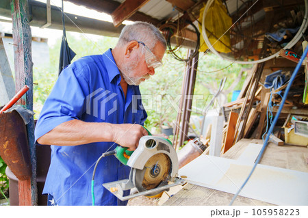 an elderly man in goggles with a circular saw 105958223