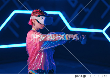 Young female gamer in pink is playing virtual reality games. VR headset and controllers. 105959536