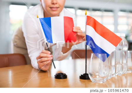 Young woman puts flags of France and Netherlands on table in office Young woman puts flags of France and Netherlands on table in office 105961470