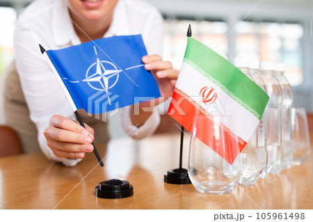 Woman secretary prepares an office for negotiations - she places flags of NATO (OTAN) and Iran table 105961498