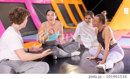 Group of enthusiastic young people sitting on trampoline and discussing upcoming jumping workout in entertainment center 105961538