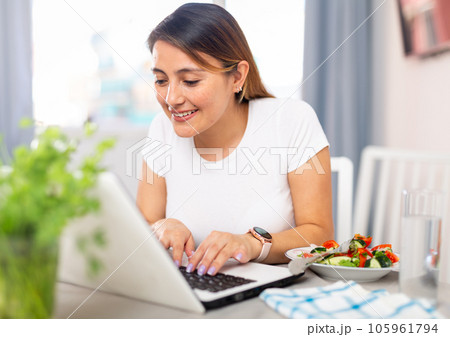 Woman working on laptop before eating vegetable salad Woman working on laptop before eating vegetable salad 105961794