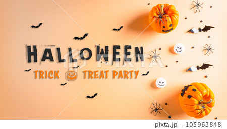 Halloween decorations made from pumpkin, paper bats, black spider and the text on pastel orange background. 105963848