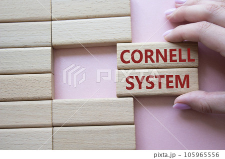 Cornell system symbol. Concept word Cornell system on wooden blocks. Businessman hand. Beautiful pink background. Business and Cornell system concept. Copy space Cornell system symbol. Concept word Cornell system on wooden blocks. Businessman hand. Beautiful pink background. Business and Cornell system concept. Copy space 105965556