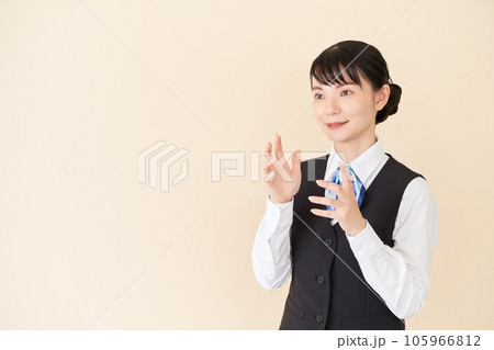 説明するベストにリボンタイの制服を着た、受付業務、事務業務の女性 説明するベストにリボンタイの制服を着た、受付業務、事務業務の女性 105966812