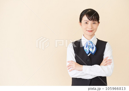 腕を組むベストにリボンタイの制服を着た、受付業務、事務業務の女性 腕を組むベストにリボンタイの制服を着た、受付業務、事務業務の女性 105966813