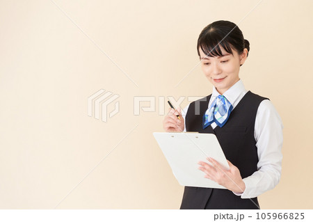 書類を書くベストにリボンタイの制服を着た、受付業務、事務業務の女性 書類を書くベストにリボンタイの制服を着た、受付業務、事務業務の女性 105966825