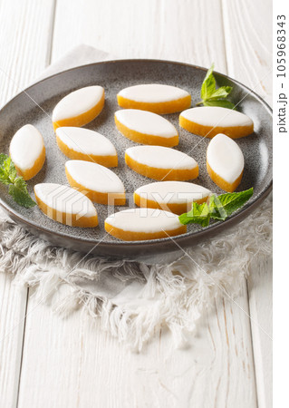 French candy Calissons consisting of pale yellow homogeneous paste of candied fruit melons and oranges and ground almonds topped with a thin layer of royal icing closeup on the plate. Vertical French candy Calissons consisting of pale yellow homogeneous paste of candied fruit melons and oranges and ground almonds topped with a thin layer of royal icing closeup on the plate. Vertical 105968343