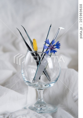 Various professional tools for eyelash extension procedure lying in wineglass with little cornflower on white sheet. Various professional tools for eyelash extension procedure lying in wineglass with little cornflower on white sheet. 105969688