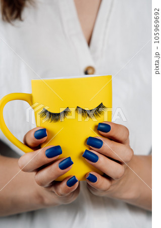 Unrecognizable woman holding cup of beverage decorated with fake eyelashes as closed eyes, sticked on outside of cup. Unrecognizable woman holding cup of beverage decorated with fake eyelashes as closed eyes, sticked on outside of cup. 105969692